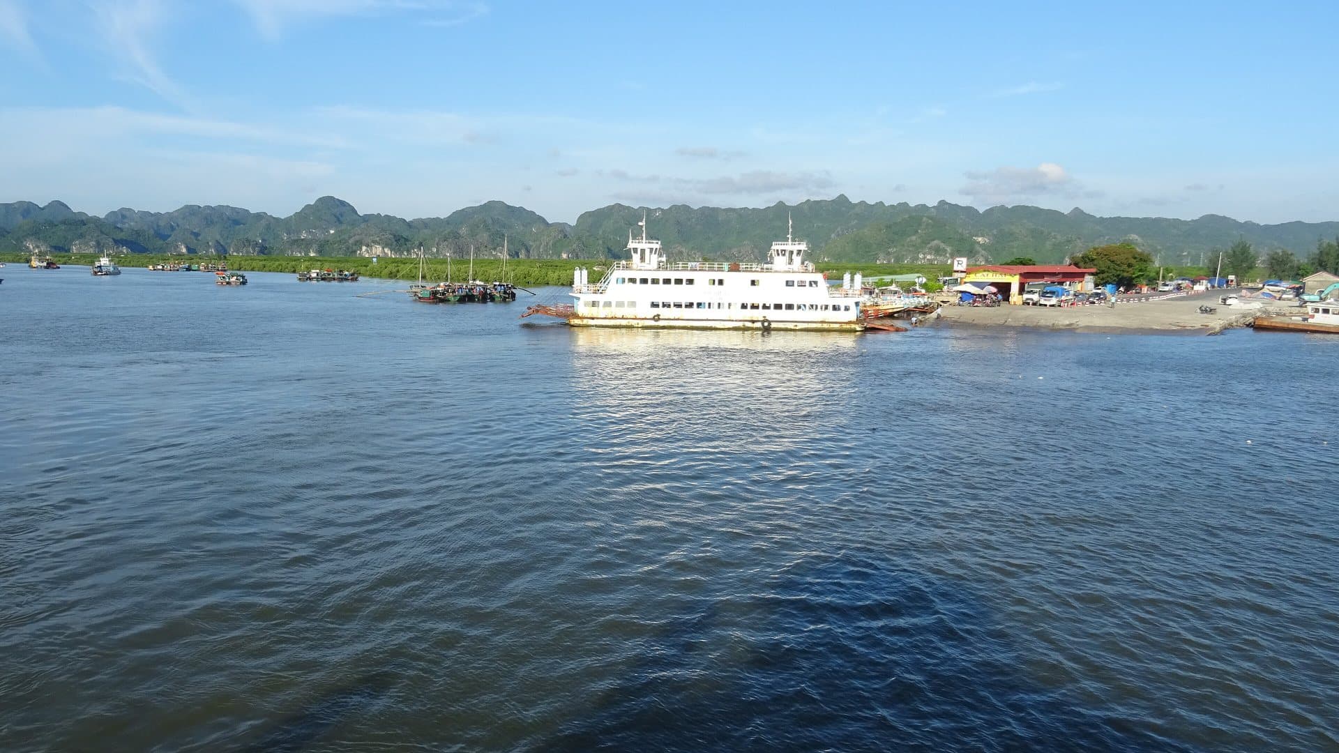 A white car ferry crossing calm water toward the karst hills of Cat Ba Island, one of the crossings on the bus-and-boat route from Hanoi
