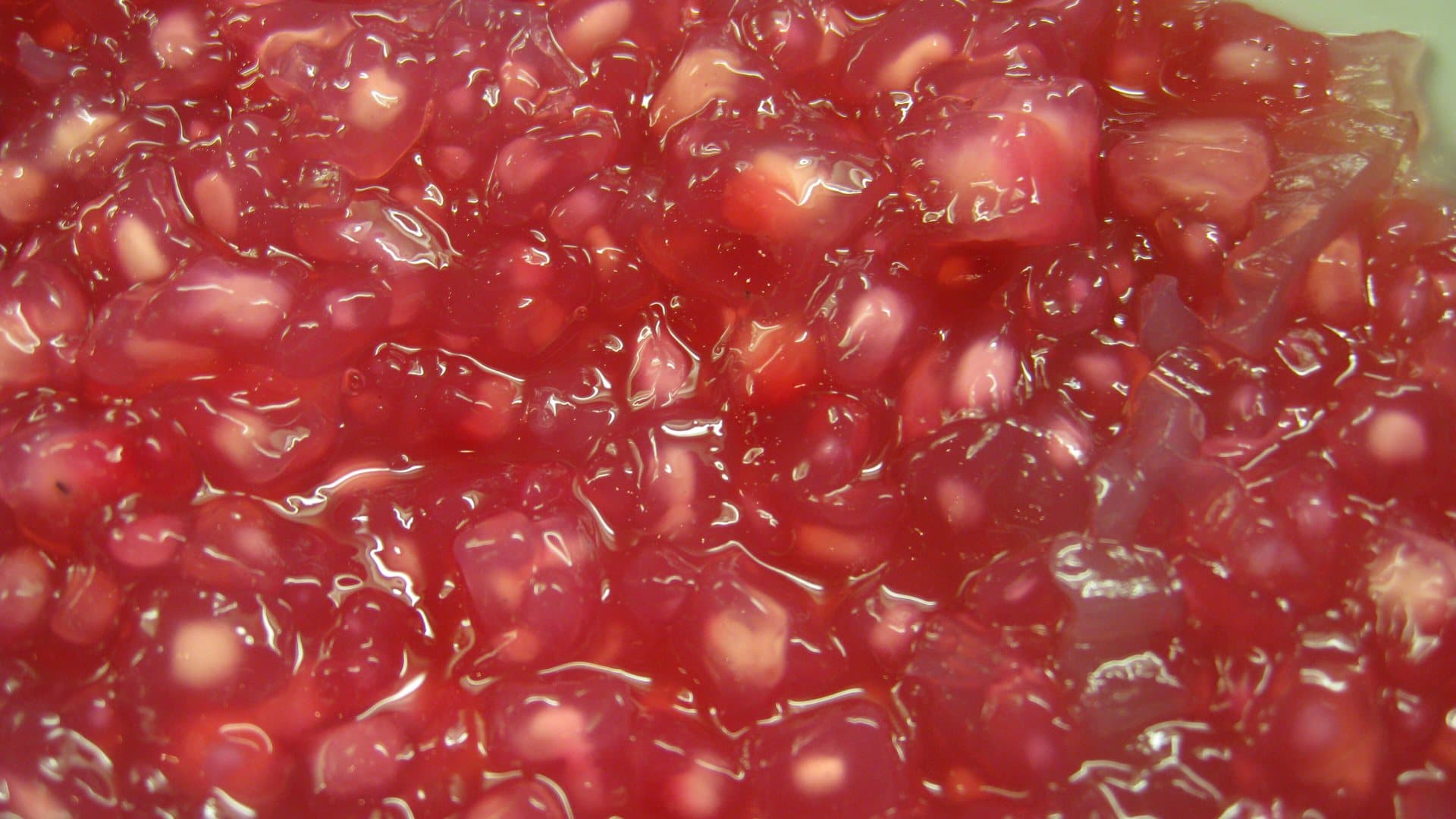 Close-up of chè hạt lựu, a Vietnamese sweet soup of ruby-red tapioca pieces shaped and coloured like pomegranate seeds, glistening in syrup