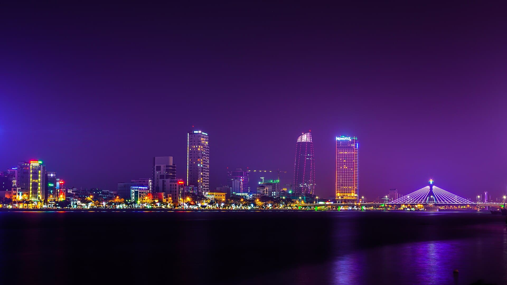 The Da Nang skyline at night, Han River reflecting Novotel Premier Han River and the cable-stayed Han River Bridge — the digital-nomad hub of central Vietnam