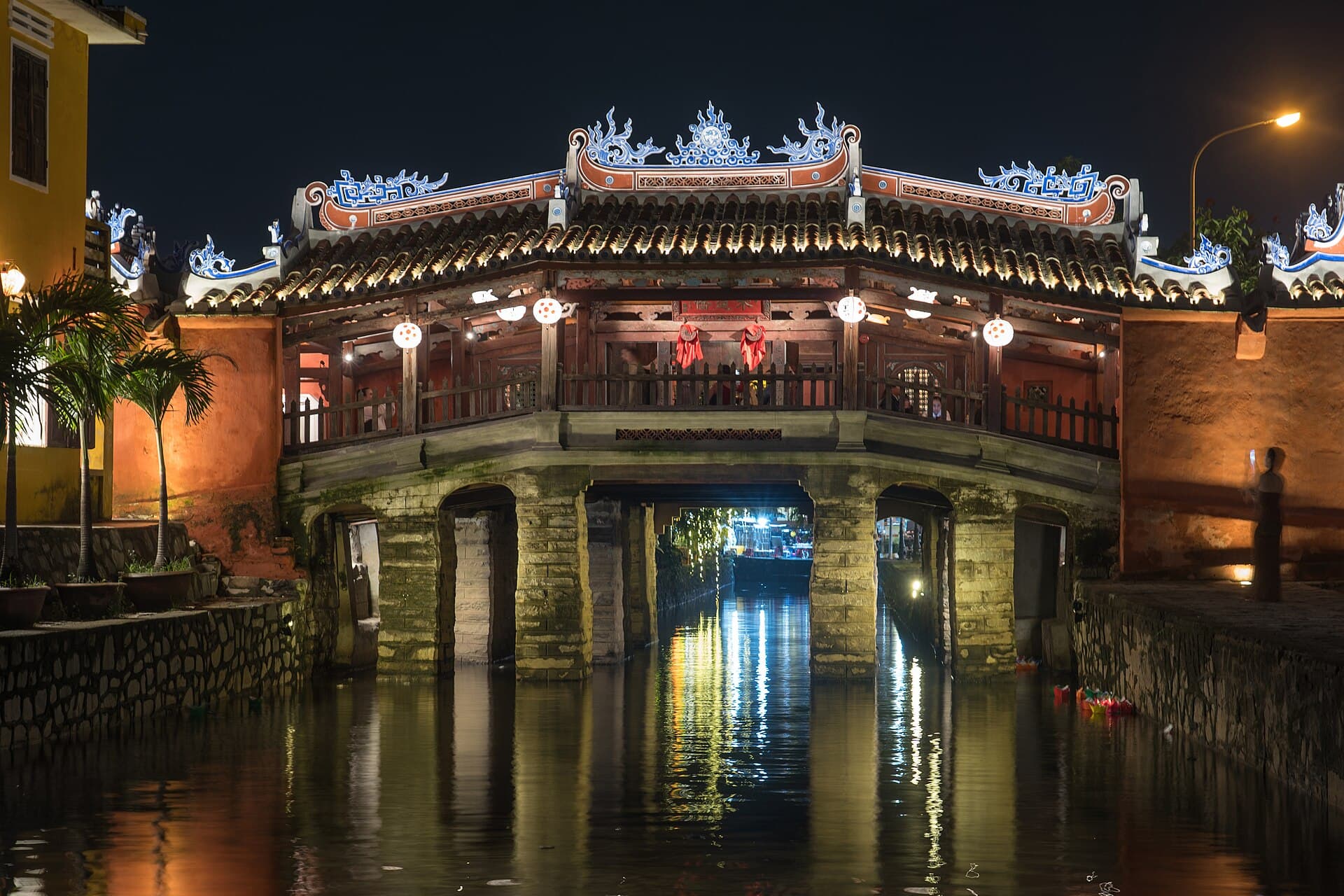 The Japanese Covered Bridge in Hoi An lit at night and reflected in the canal — the kind of cultural-icon experience that runs ~25% cheaper in Vietnam than its Thai equivalent