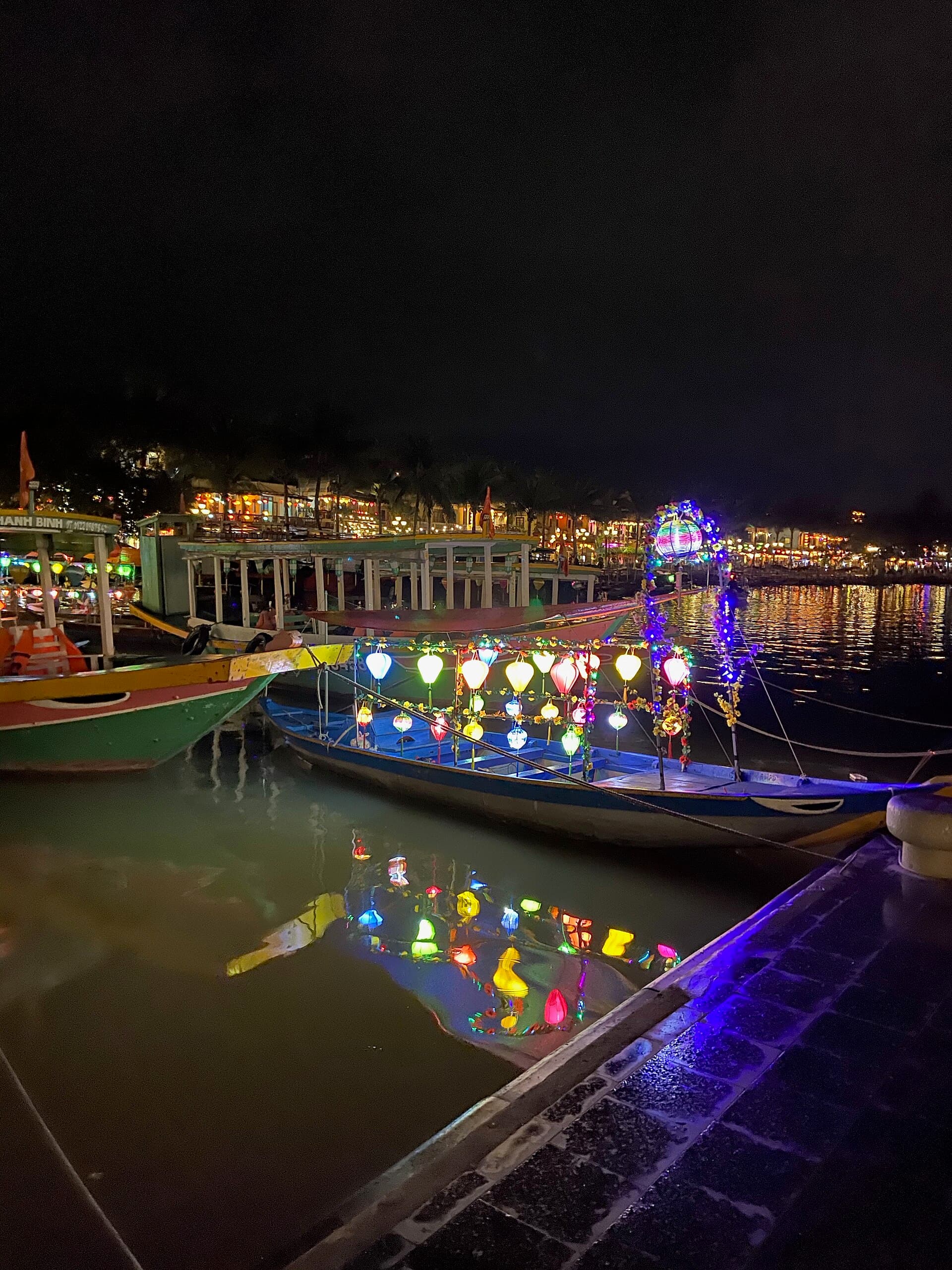 Wooden boats hung with colorful lanterns reflected in the Thu Bon river at night in Hoi An — the centerpiece of a 2-week Vietnam itinerary's central-coast leg