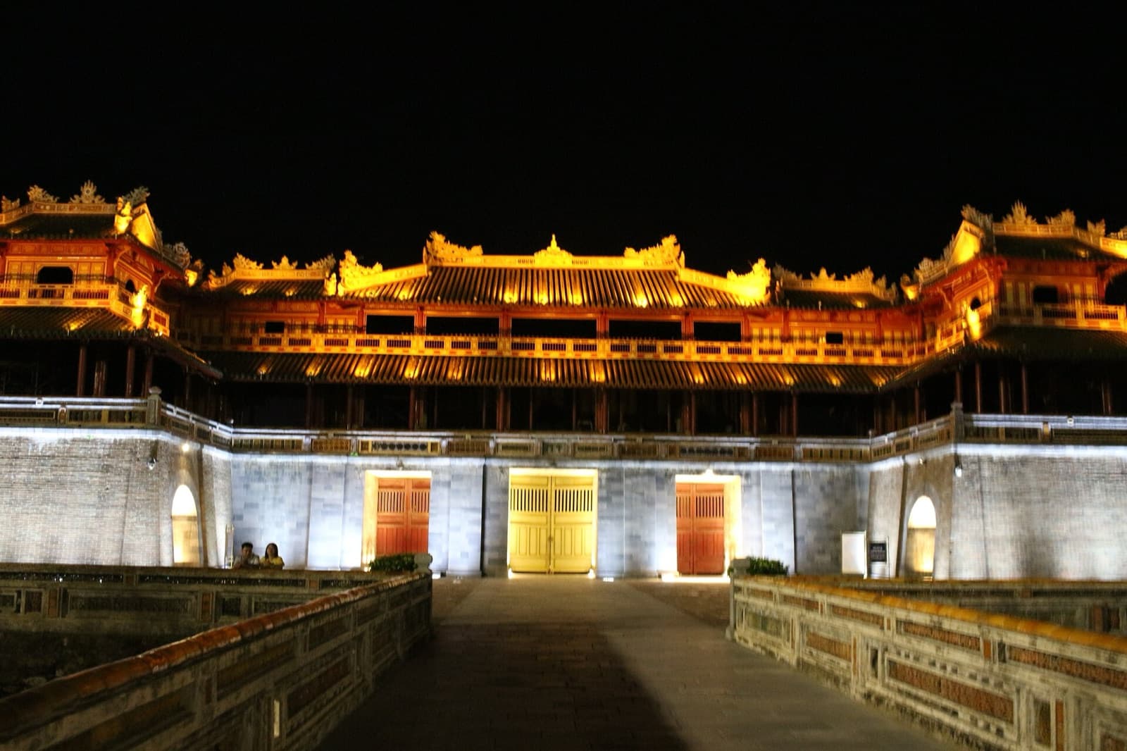 The Meridian Gate of the Hue Imperial Citadel floodlit gold against a night sky, its yellow central door and flanking red doors lit from below — the main ticketed entrance to the UNESCO site