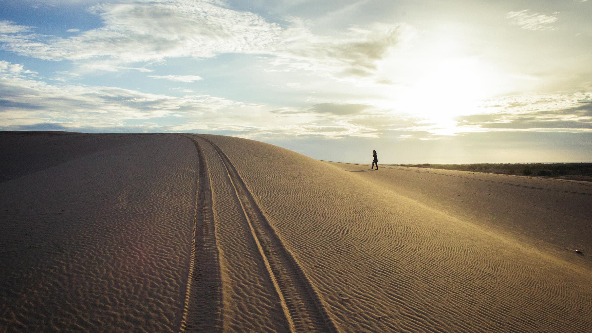 Low sun over the White Sand Dunes north of Mui Ne, with vehicle tracks running along the crest of the dune and a single walker silhouetted on the ridge