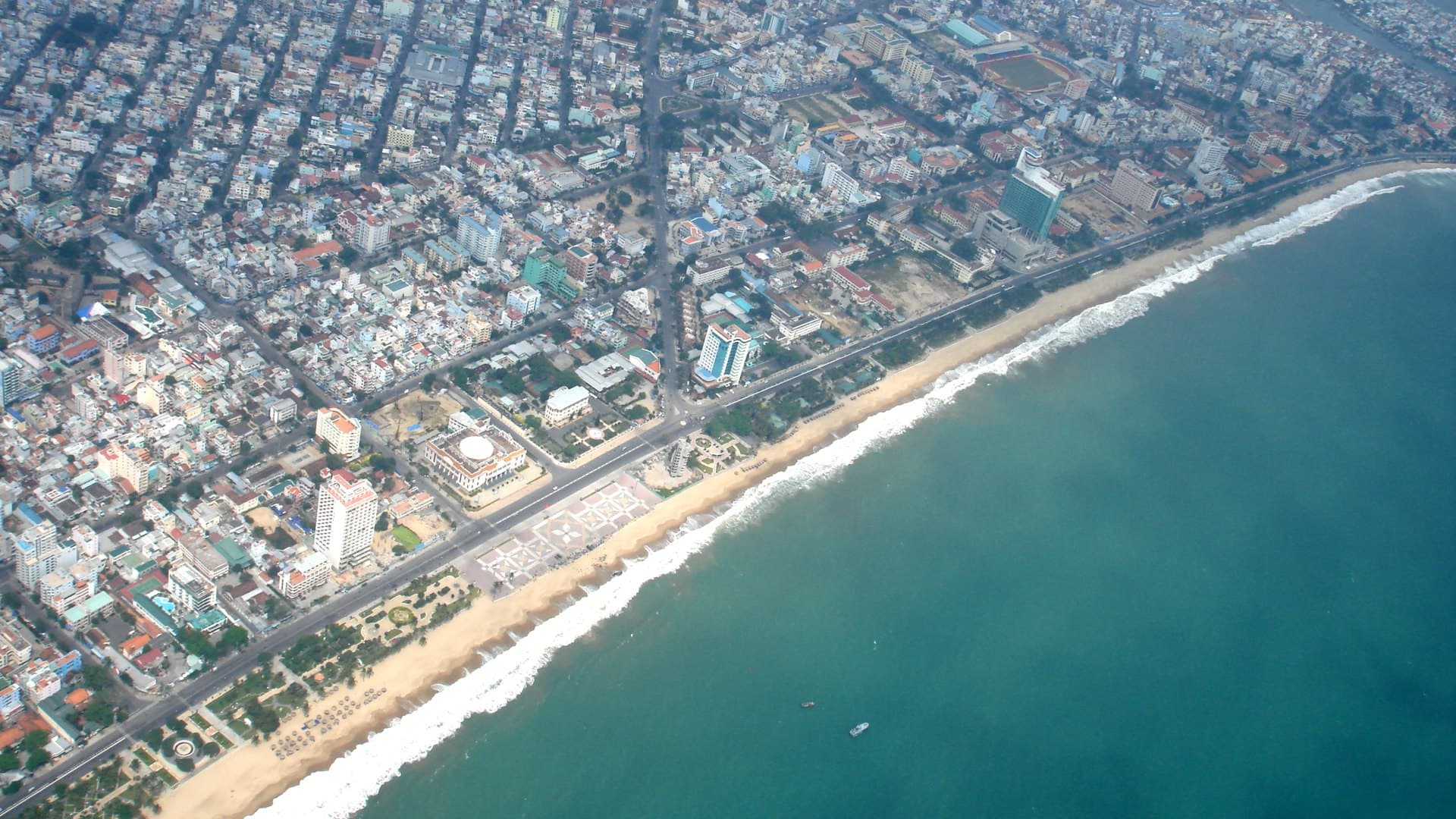 Seen from high above, Nha Trang's dense city blocks and hotels line a long curve of sandy beach edged with white surf and turquoise sea.