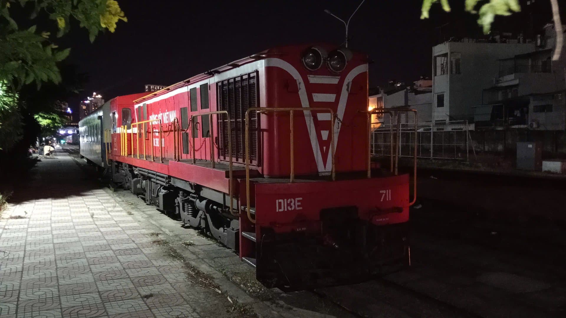 A red Vietnam Railways D13E diesel locomotive at the platform of Nha Trang station at night, the southern end of the Da Nang to Nha Trang rail journey