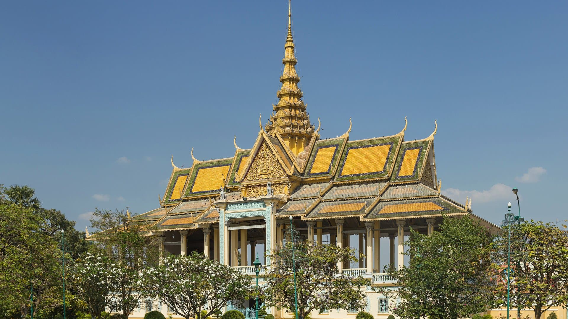 The golden spire and tiered roofs of the Chanchhaya Pavilion at the Royal Palace in Phnom Penh under a blue sky