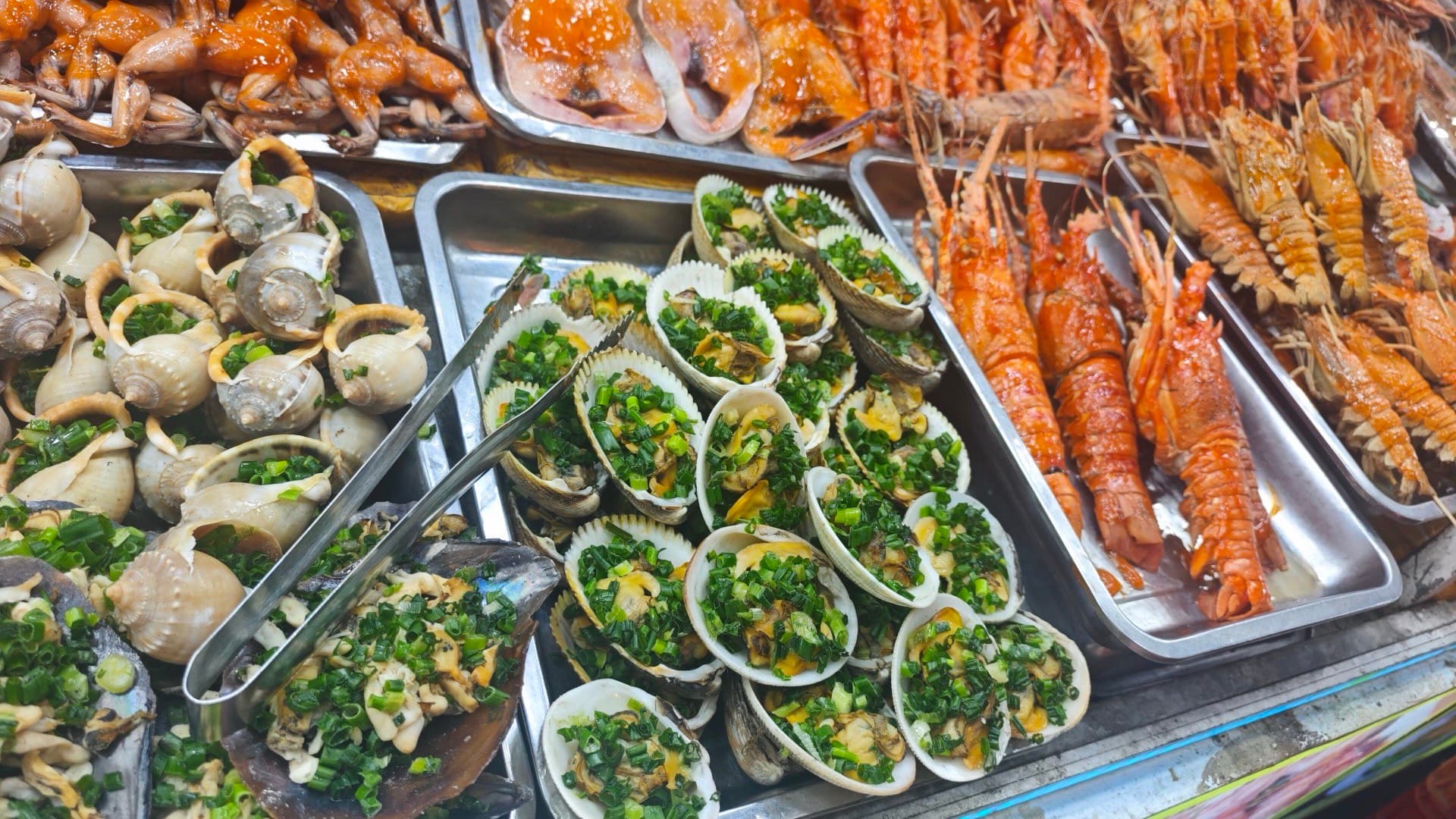 Trays of scallops topped with chopped spring onion, sea snails and orange slipper lobsters on display at a seafood stall in Phu Quoc.