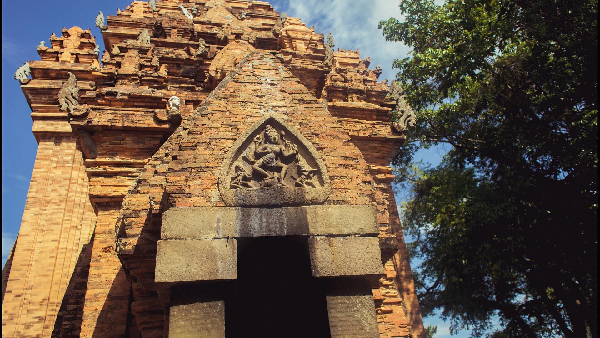 The carved brick doorway and tower of the Po Nagar Cham temple in Nha Trang, under a blue sky with trees beside it