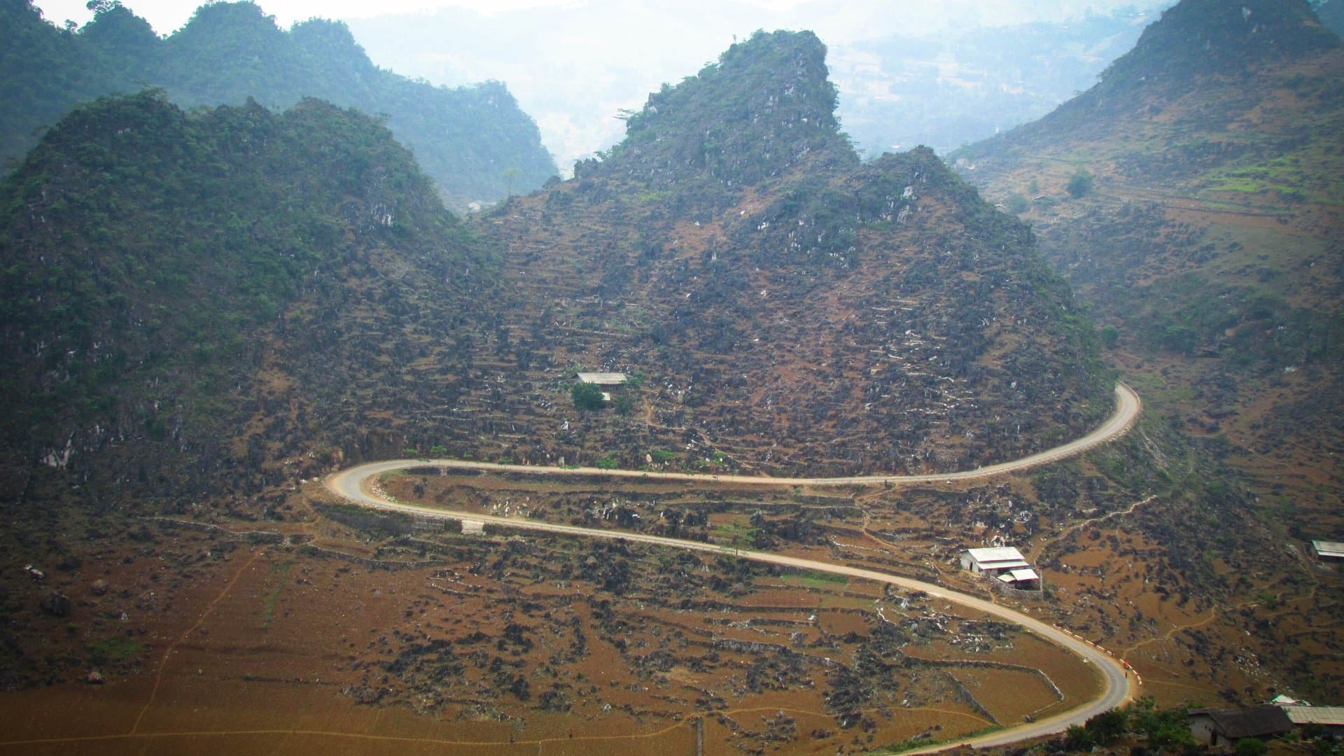 A road winding in tight curves between steep grey limestone peaks on the way to Dong Van in Ha Giang