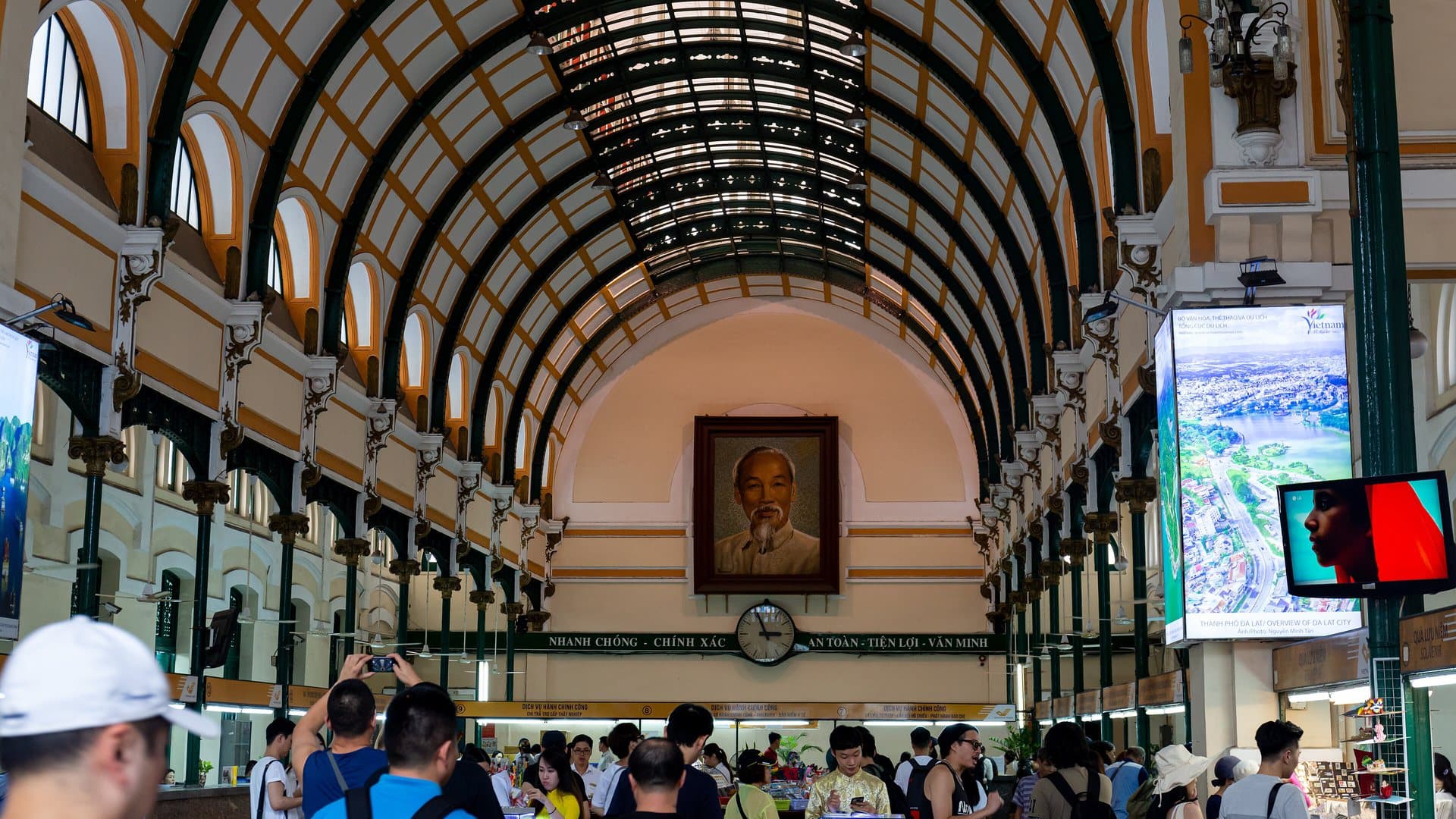 The arched iron-and-glass hall of Saigon Central Post Office, with a portrait of Ho Chi Minh above the counters and visitors below, a stop on the first day in Ho Chi Minh City