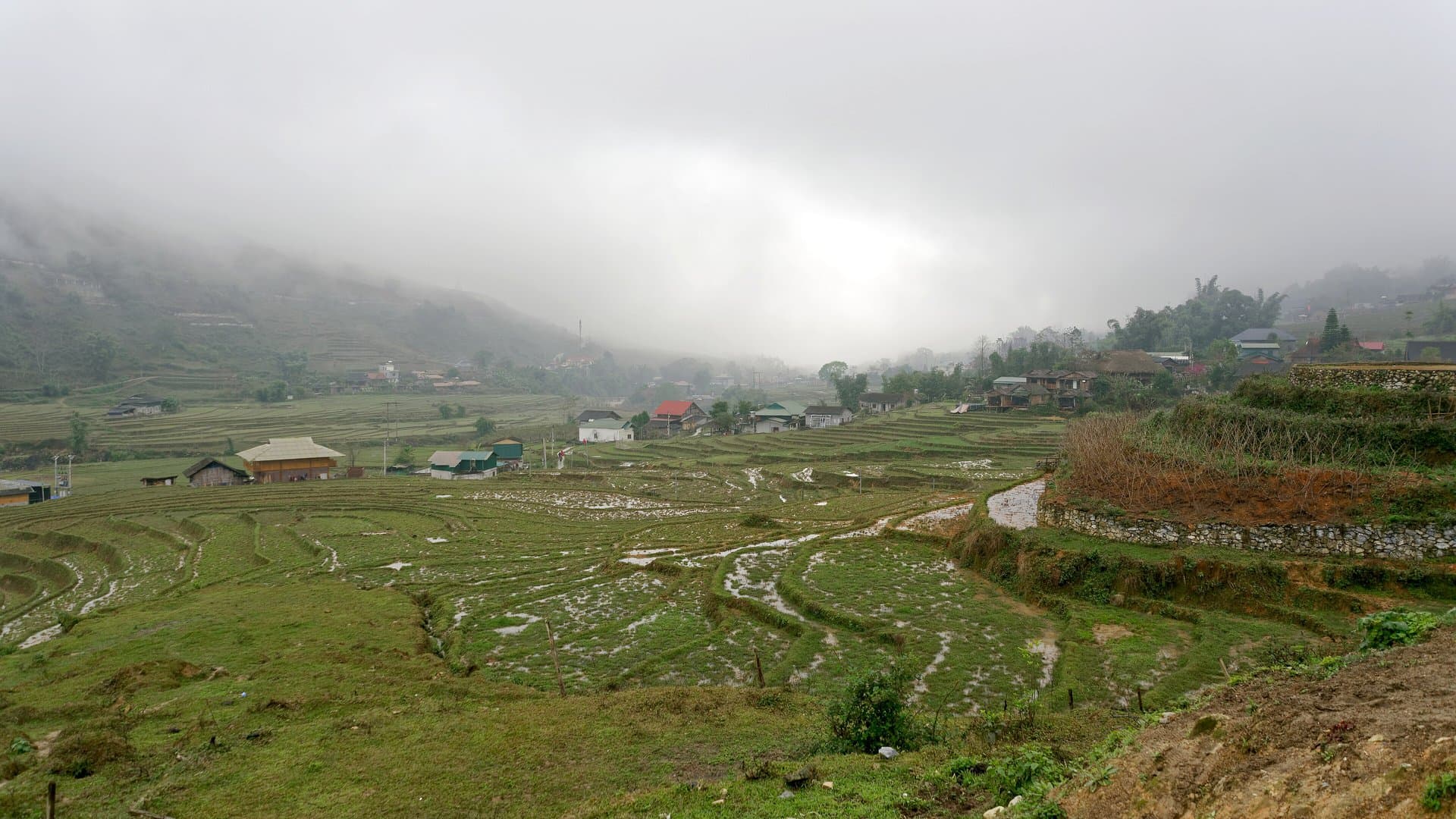 Terraced rice fields in Lao Chai, below Sa Pa, fallow for winter under low mist and grey cloud, with village houses on the hillside