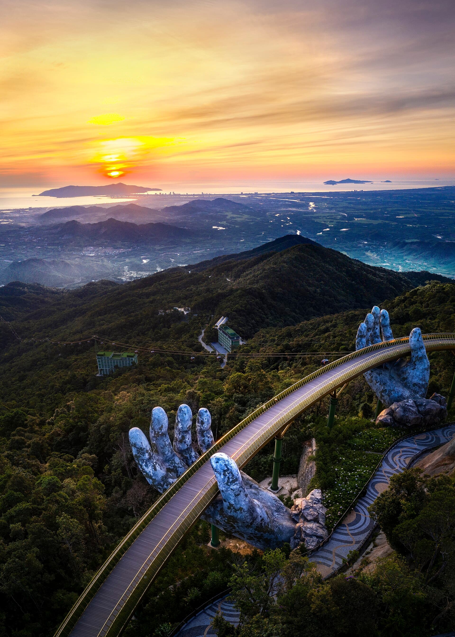 The Golden Bridge (Cau Vang) held by giant stone hands at Ba Na Hills above Da Nang, sunset over the South China Sea — the iconic image of a Vietnam grand-tour itinerary