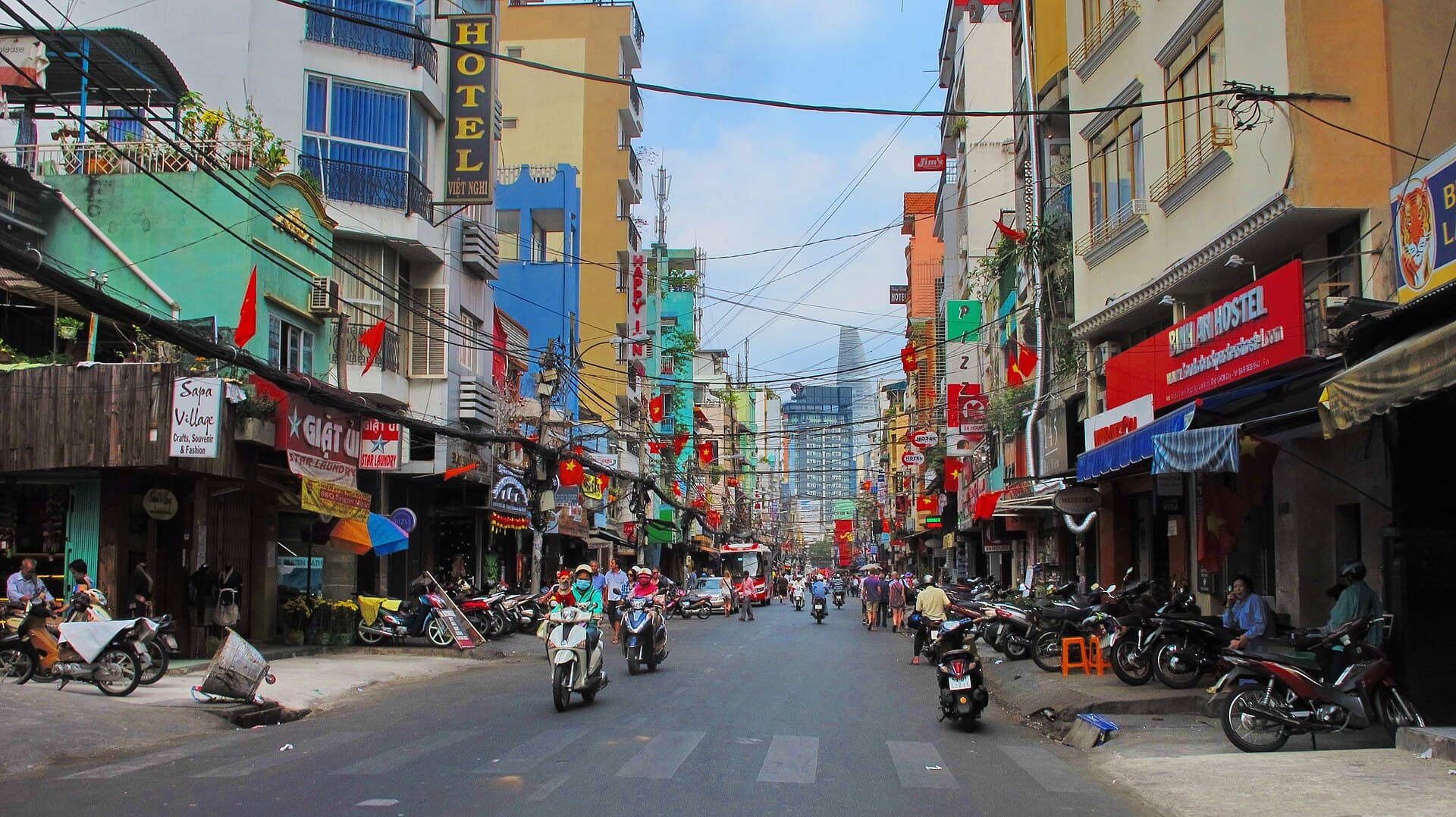 Mini-hotels, hostels and guesthouses stacked along Bui Vien in Ho Chi Minh City's Pham Ngu Lao backpacker quarter, motorbikes parked along both kerbs