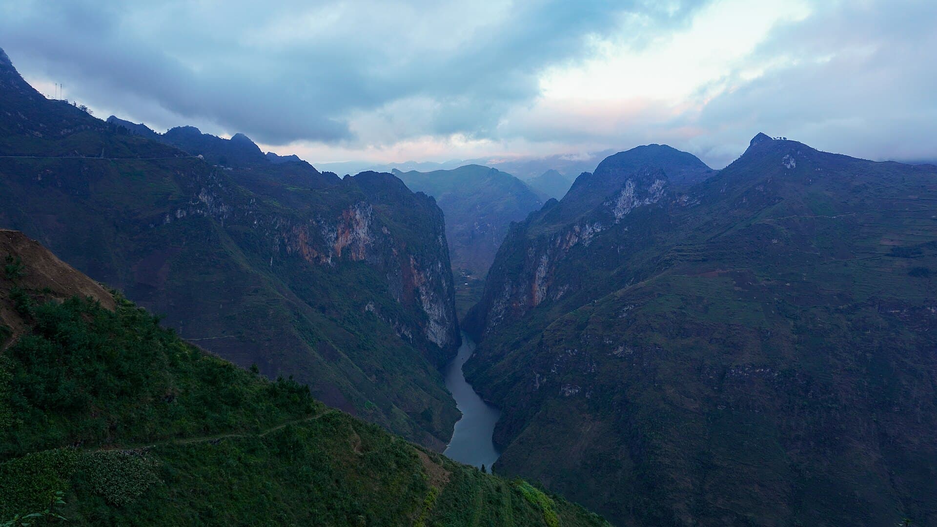 The Nho Que river threading the Tu San canyon below Ma Pi Leng Pass at dusk, with the pass road cut into the ridge on the left