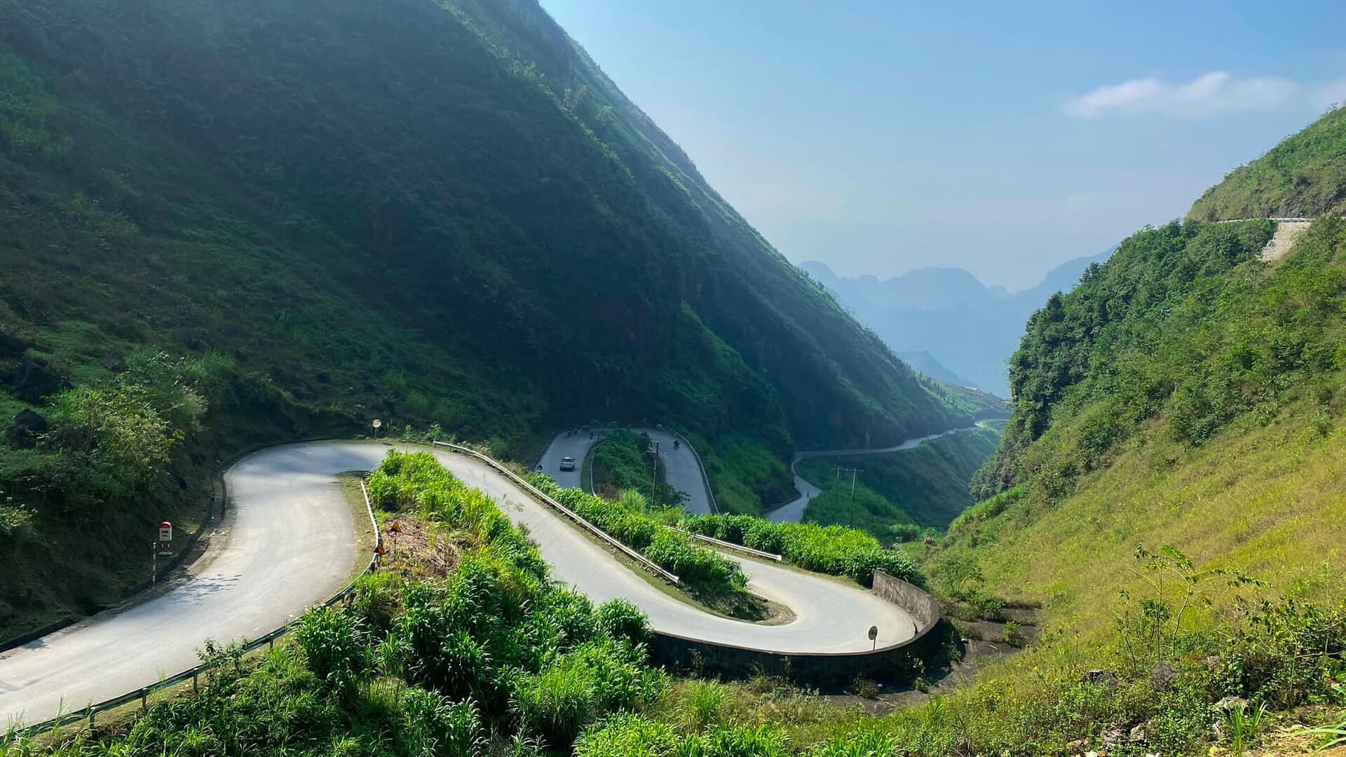 The hairpin switchbacks of the Tham Ma pass stacking down a green valley on the road up to Dong Van, with karst peaks fading into haze