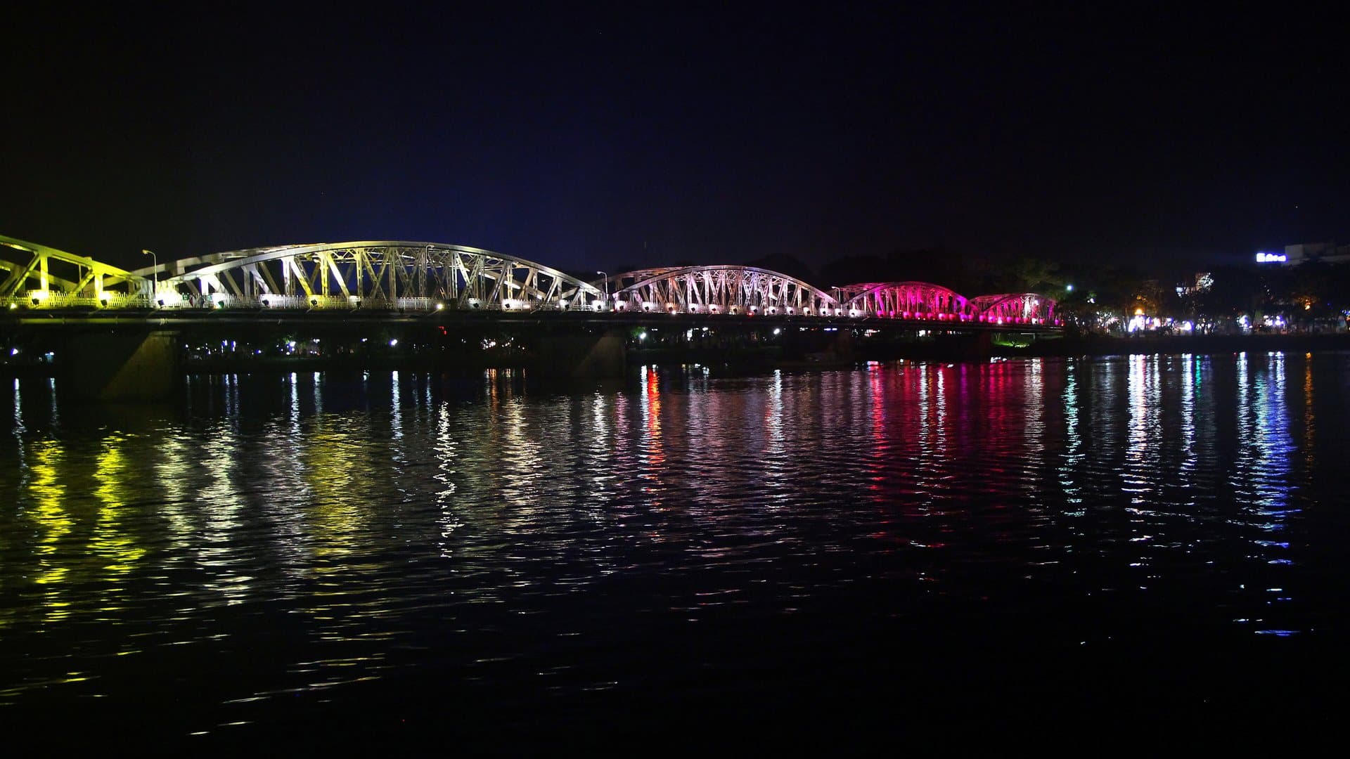 Truong Tien Bridge lit in changing colours across the Perfume River at night in Hue, with the lights reflected in the water beside the south-bank riverfront